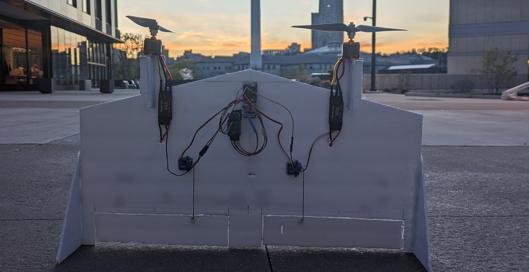A twin-motor foam flying wing with its wiring exposed, at sunset